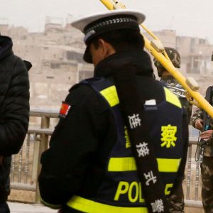 A police officer checks the identity card of a man as security forces keep watch in a street in Kashgar