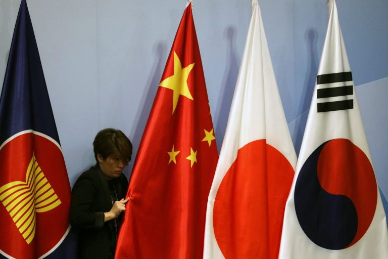 An officer adjusts China's national flag before the ASEAN Plus Three (APT) Summit in Singapore