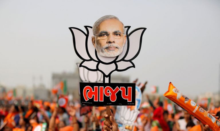 FILE PHOTO: A supporter holds up a cut-out of lotus, the election symbol of India's ruling BJP, with an image of PM Modi during a campaign meeting addressed by Modi ahead of Gujarat state assembly election in Kalol