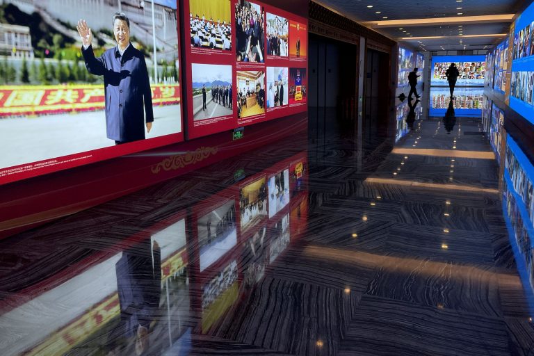 Images of Chinese President Xi Jinping are seen on an exhibition about Tibet Autonomous Region, while people walk on a hall at the foreign ministry building in Beijing