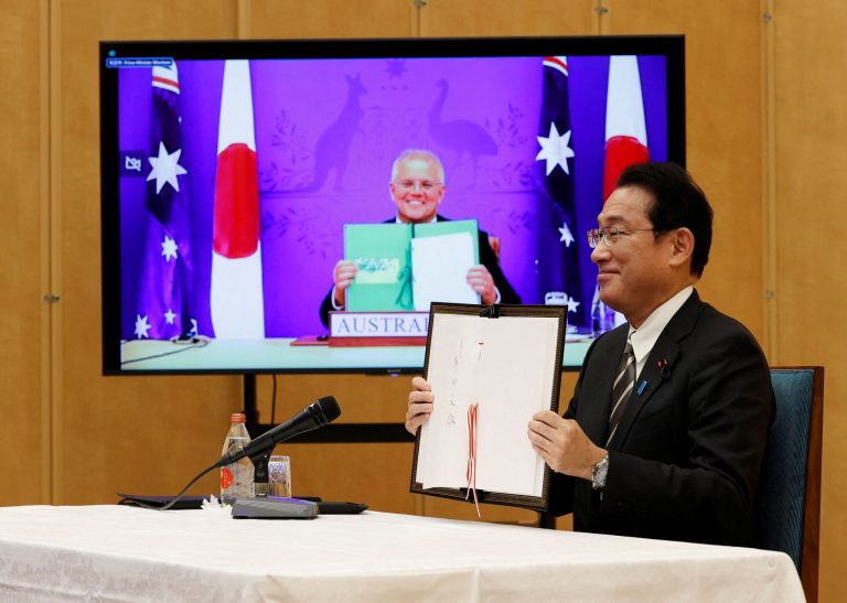 Japan's Prime Minister Fumio Kishida and Australia's Prime Minister Scott Morrison show off signed documents during their video signing ceremony of the bilateral reciprocal access agreement in Tokyo