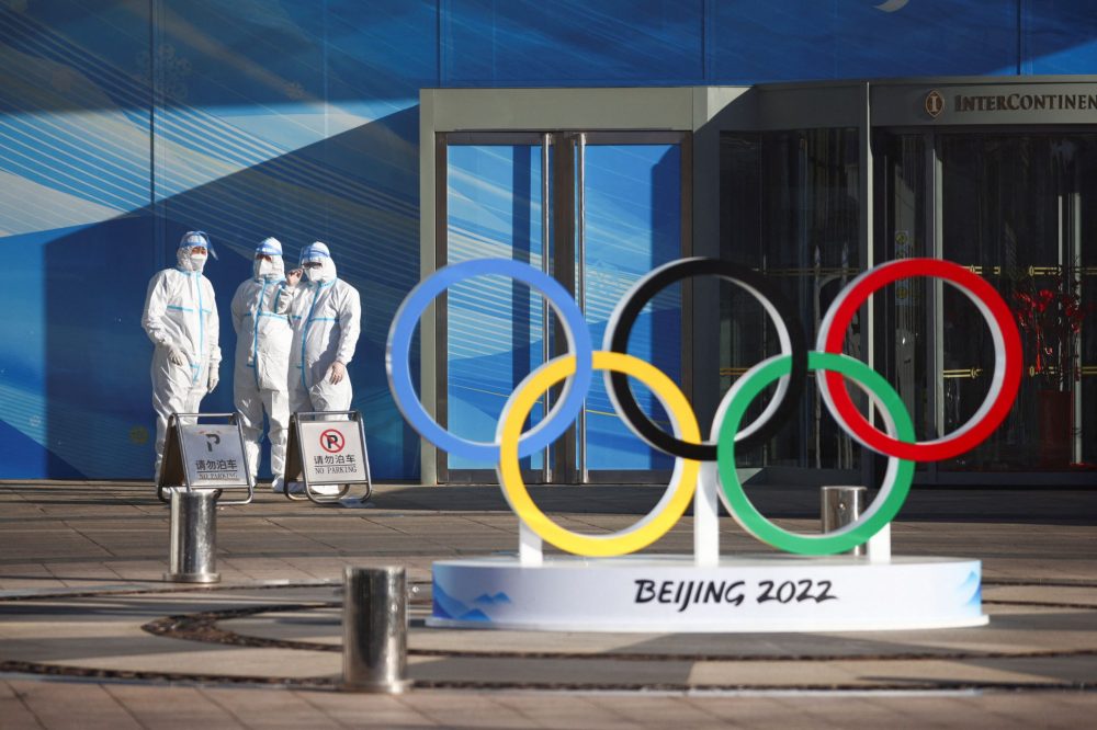 Staff in PPE stand next to the olympic rings inside the Olympic bubble near the National Stadium in Beijing